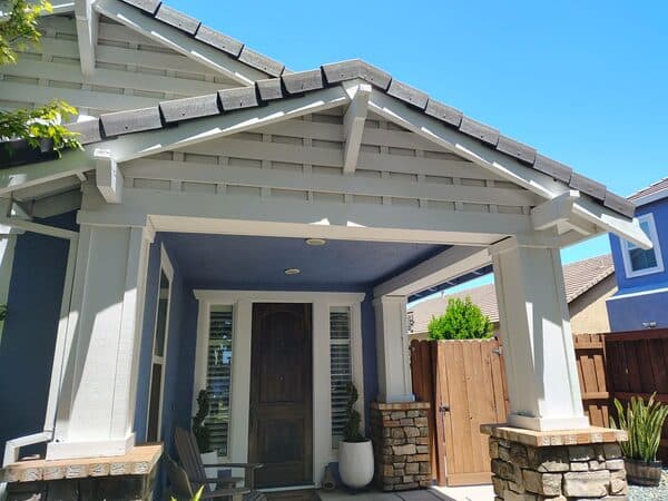Home Construction by DCB Construction Sacramento Professionally remodeled exterior of a front patio walkway with half stone pillars and half white wood pillars, newly tiled roof blue exteiro and ceiling to the home in Sacramento CA