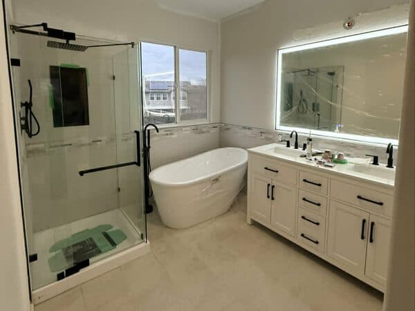 Construction Project by DCB Construction Sacramento Newly installed shower and bathtub, mirror with rimmed lighting and a his and her white countertop with 2 sinks, white with black metal handles and faucets in Sacramento CA