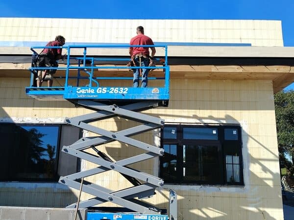 Commercial Construction by DCB Construction Sacramento 2 workers working on the exterior of a commercial building, on a lift working on the edge of the roof in Sacramento CA